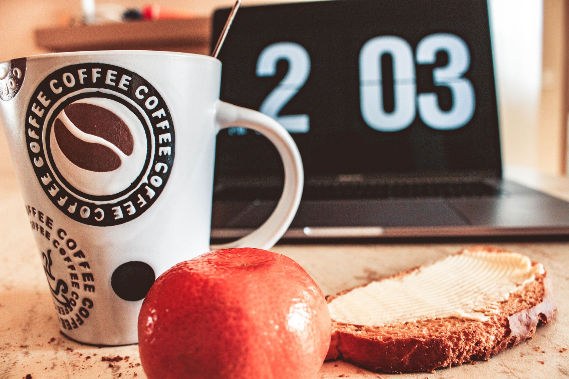 Un petit-déjeuner simple avec un café, du pain et un ordinateur portable, installé pour une session de travail à domicile.