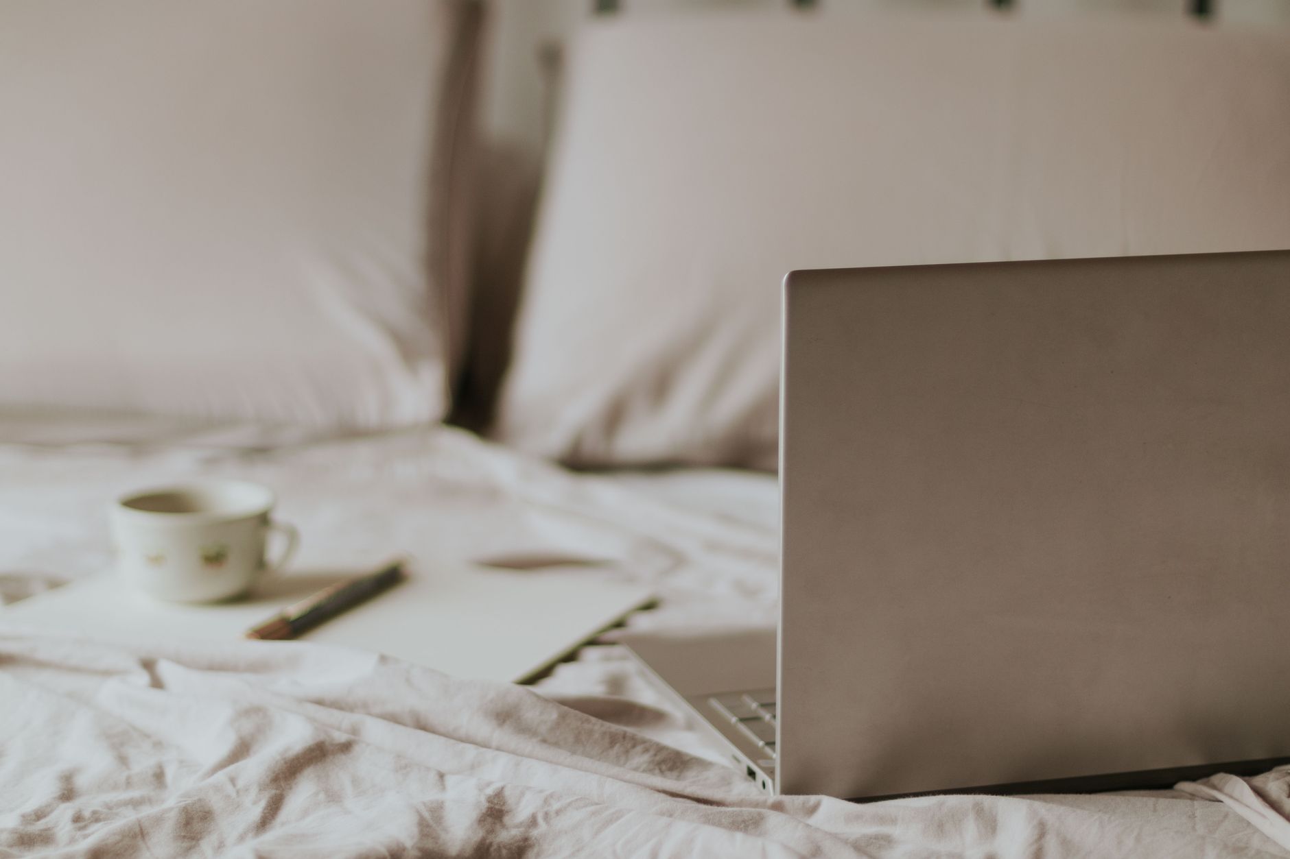 Espace de travail à domicile avec ordinateur portable, tasse de café et bloc-notes sur un lit.